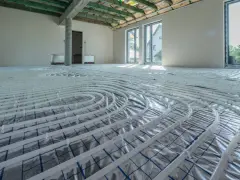 Instalacja ogrzewania podłogowego w nowym domu. Rury ułożone na folii izolacyjnej, gotowe do zalania betonem. To przyszłe oszczędności na koszt ogrzewania podłogowego.