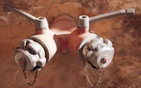 Czerwony hydrant podziemny z dwoma metalowymi wylotami i uchwytami, gotowy do akcji.