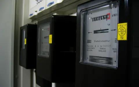Szereg liczników energii elektrycznej, każdy z wyświetlaczem pokazującym zużycie. Jeden z nich ma żółtą naklejkę z napisem "silnik inwerterowy".