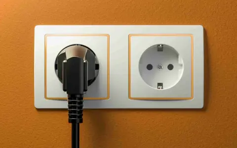 Dwa gniazdka elektryczne na pomarańczowej ścianie. Jedno z nich jest puste, drugie z wtyczką. Zastanawiasz się, jakie gniazdka w Egipcie?