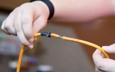 Dłonie trzymają uszkodzony przewód elektryczny, odsłaniając jego żyły. Różne rodzaje przewodów elektrycznych wymagają odpowiedniej naprawy.