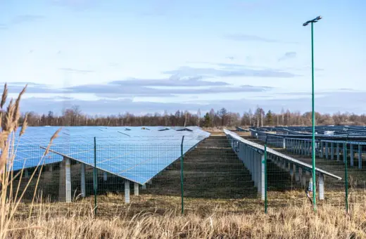 Rozległa farma fotowoltaiczna z rzędami paneli słonecznych na tle nieba z chmurami.