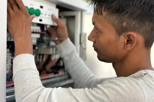 Młody mężczyzna pracuje przy skrzynce elektrycznej, montując moduł. To dobry początek, by dowiedzieć się, jak zostać elektrykiem.