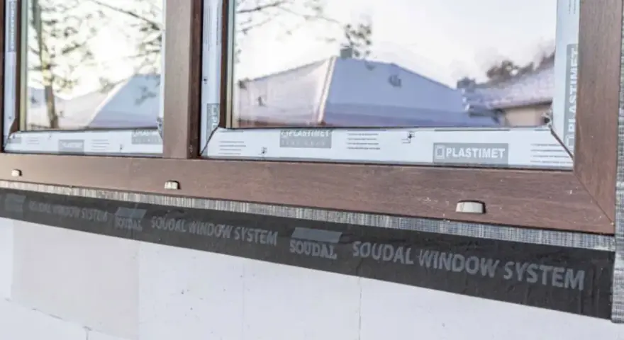 Ciepły montaż okien z użyciem taśm Soudal Window System. Brązowa rama okienna na tle białego pustaka.