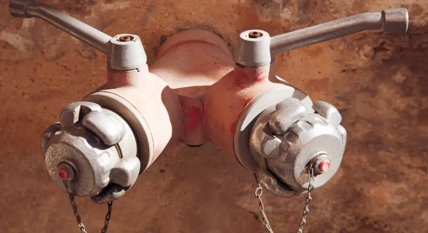 Czerwony hydrant podziemny z dwoma metalowymi wylotami i uchwytami, gotowy do akcji.