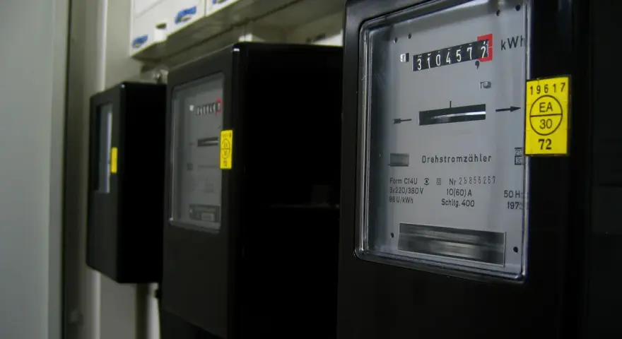Szereg liczników energii elektrycznej, każdy z wyświetlaczem pokazującym zużycie. Jeden z nich ma żółtą naklejkę z napisem "silnik inwerterowy".