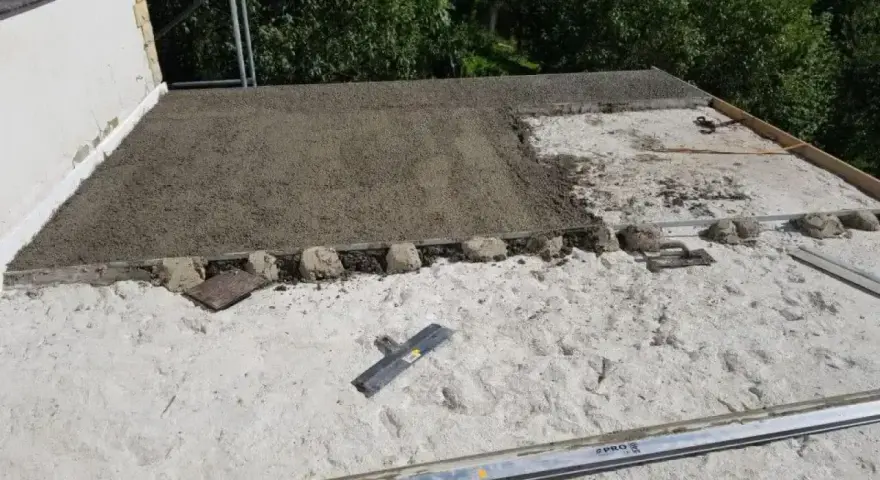 Budowa dachu z wykorzystaniem styrobetonu. Widać świeżą warstwę materiału, a obok narzędzia do jego obróbki. Prawidłowe styrobeton proporcje są kluczowe dla trwałości.