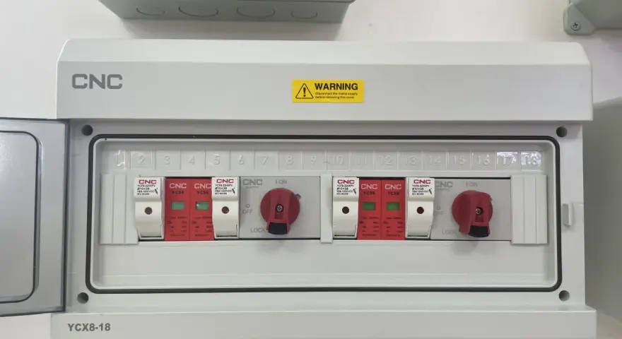 Biała skrzynka elektryczna z czerwonymi przełącznikami i numerowanymi slotami.