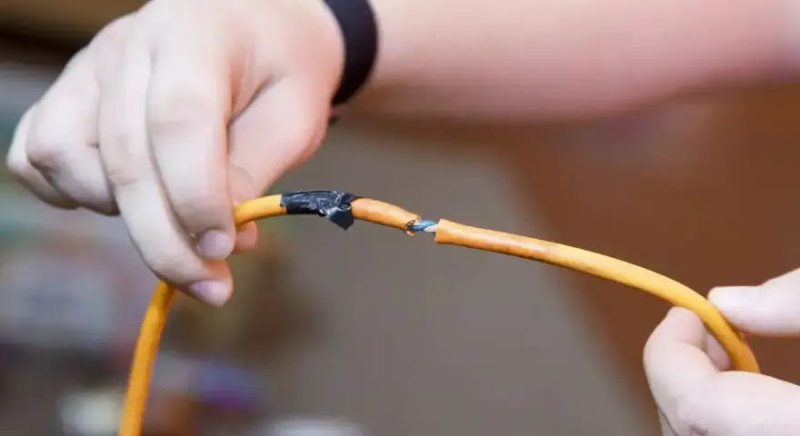 Dłonie łączące pomarańczowy kabel, pokazując, jak połączyć kable bez lutowania. Izolacja jest nacięta, a przewody odsłonięte.